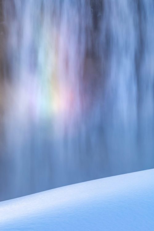 A rainbow forms from the spray of a waterfall catching the sunset light Detifoss, Iceland