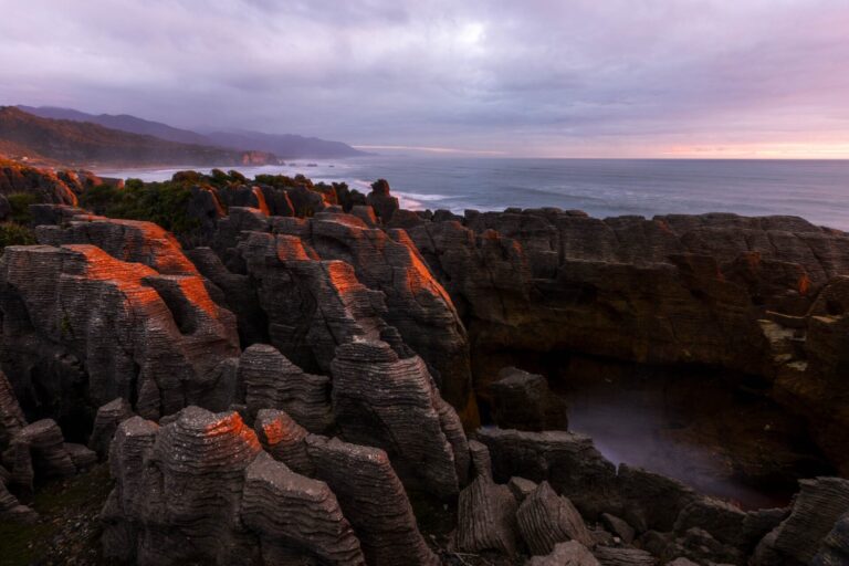 The famous Pancake Rocks at sunset with just enough swell and tide to give a bit of spray through the blowhole Punakaiki rocks, pancake rocks, New Zealand, west coast