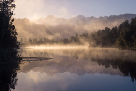 Morning fog illuminated by sunrise at Lake Matheson New Zealand, Lake Matheson